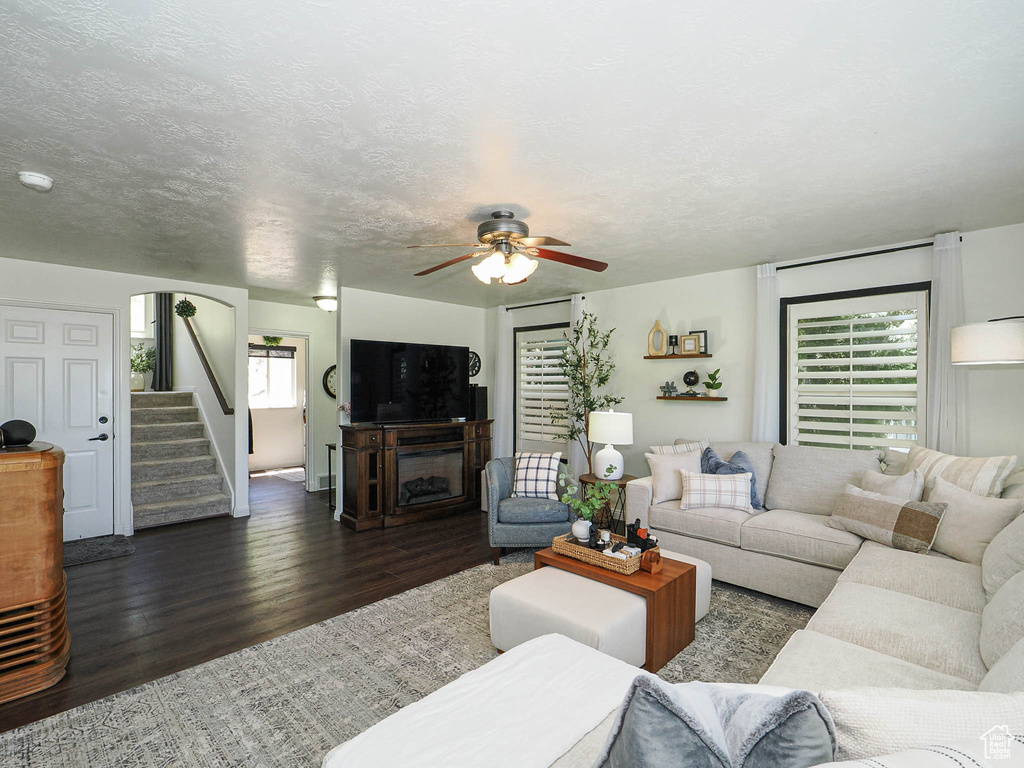 Living room with dark wood finished floors, ceiling fan, stairway, and a fireplace