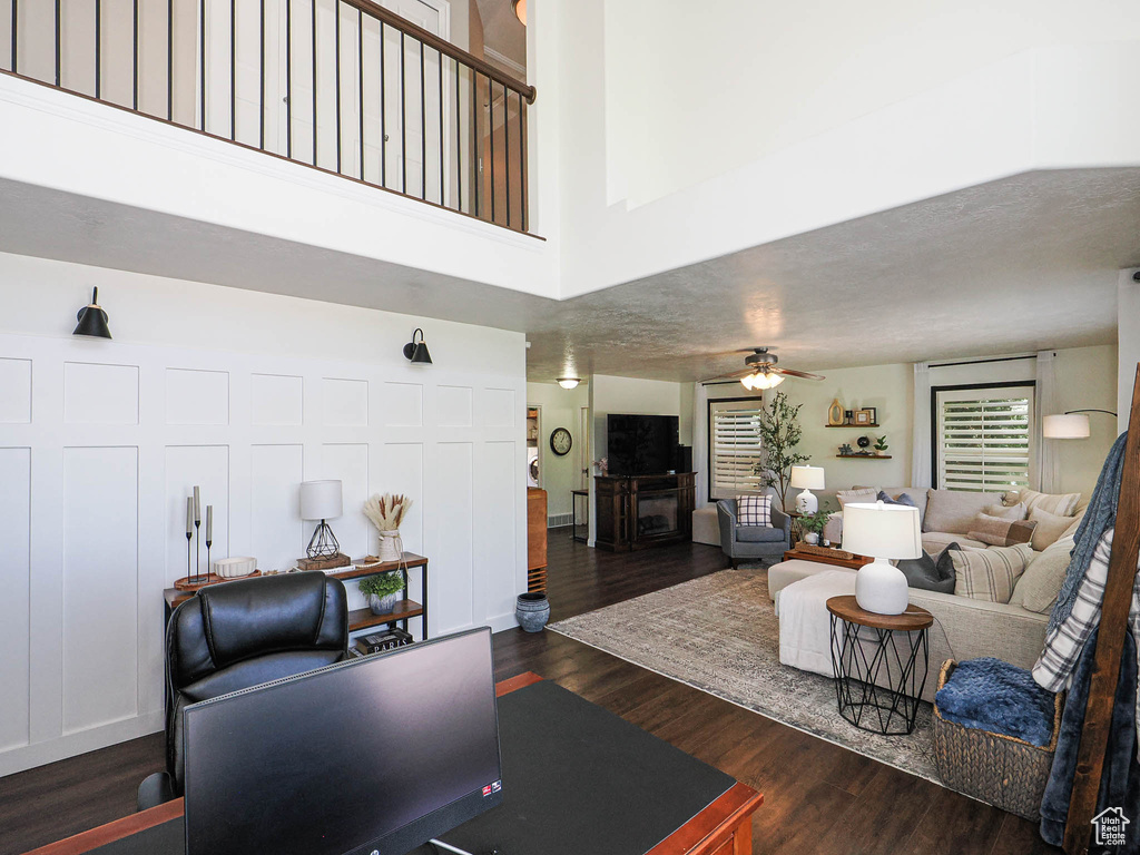 Living area with a ceiling fan, dark wood-style flooring, and a towering ceiling