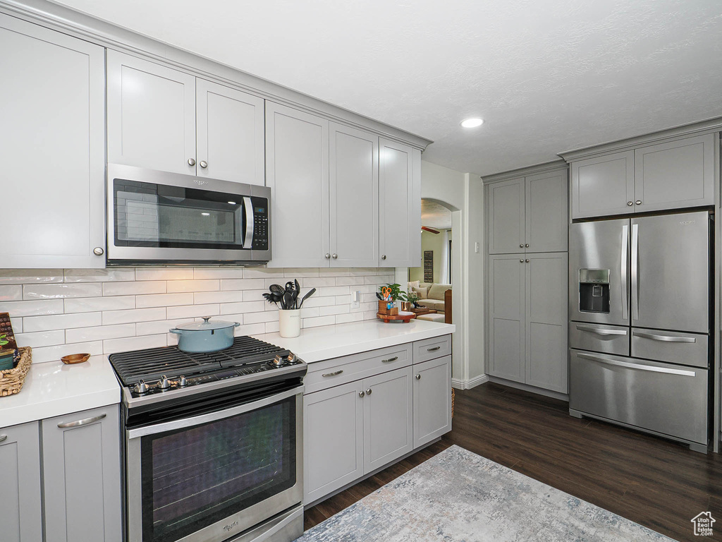 Kitchen with stainless steel appliances, gray cabinetry, dark wood finished floors, light countertops, and backsplash