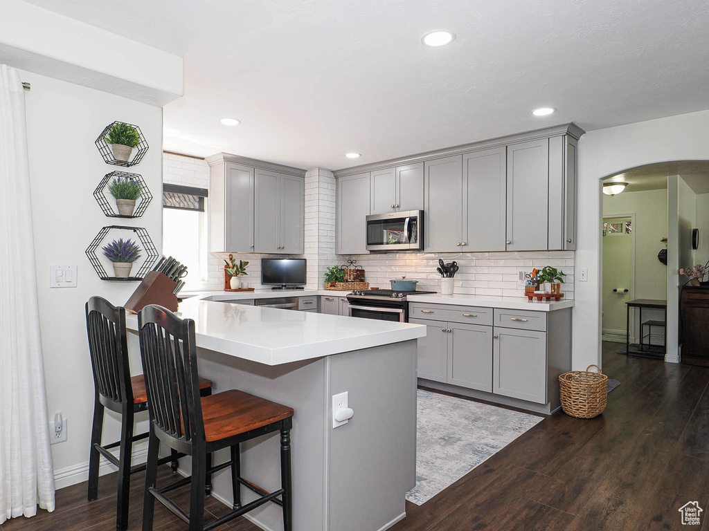 Kitchen featuring gray cabinetry, stainless steel appliances, a kitchen bar, arched walkways, and recessed lighting