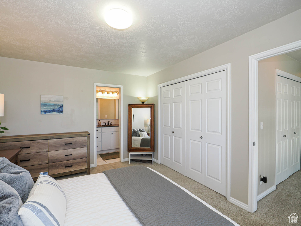 Bedroom featuring light carpet, ensuite bathroom, a textured ceiling, and a closet