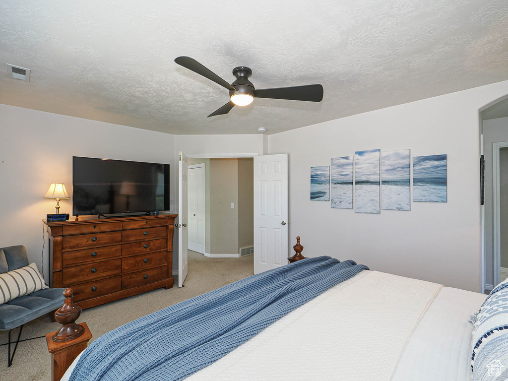 Bedroom with light colored carpet, ceiling fan, and a textured ceiling
