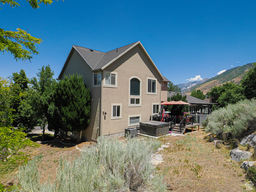 Back of house with stucco siding, a hot tub, and a deck with mountain view
