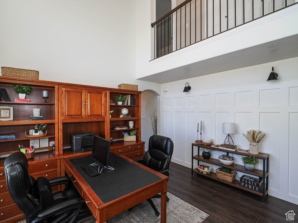 Home office featuring arched walkways, a high ceiling, and dark wood finished floors