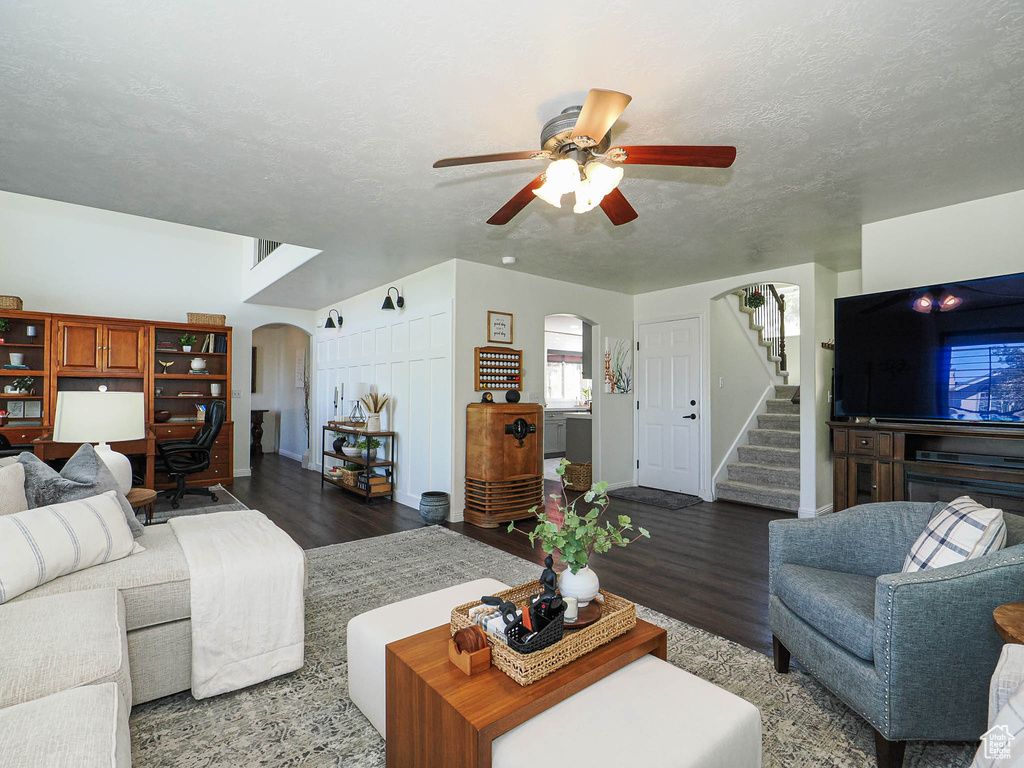 Living room featuring arched walkways, wood finished floors, a ceiling fan, stairs, and a textured ceiling
