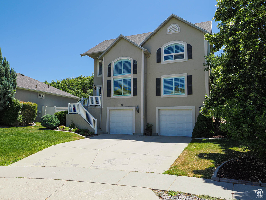 View of front of property featuring an attached garage, stucco siding, driveway, a front yard, and stairway