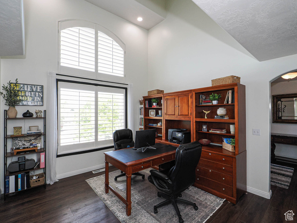 Office area with dark wood-type flooring, high vaulted ceiling, arched walkways, and recessed lighting