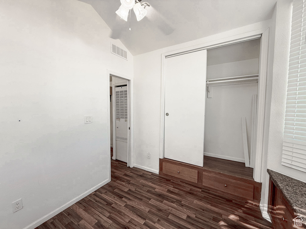 Unfurnished bedroom featuring dark wood-style flooring, vaulted ceiling, a closet, and a ceiling fan
