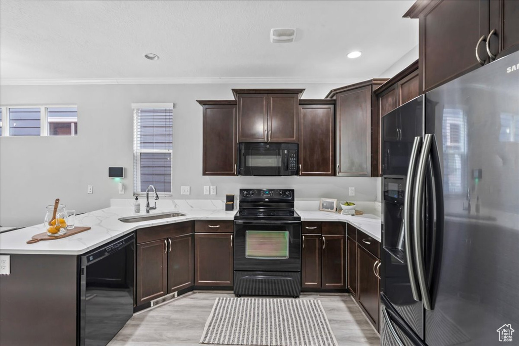 Kitchen featuring black appliances, a peninsula, light wood-style floors, crown molding, and dark brown cabinetry