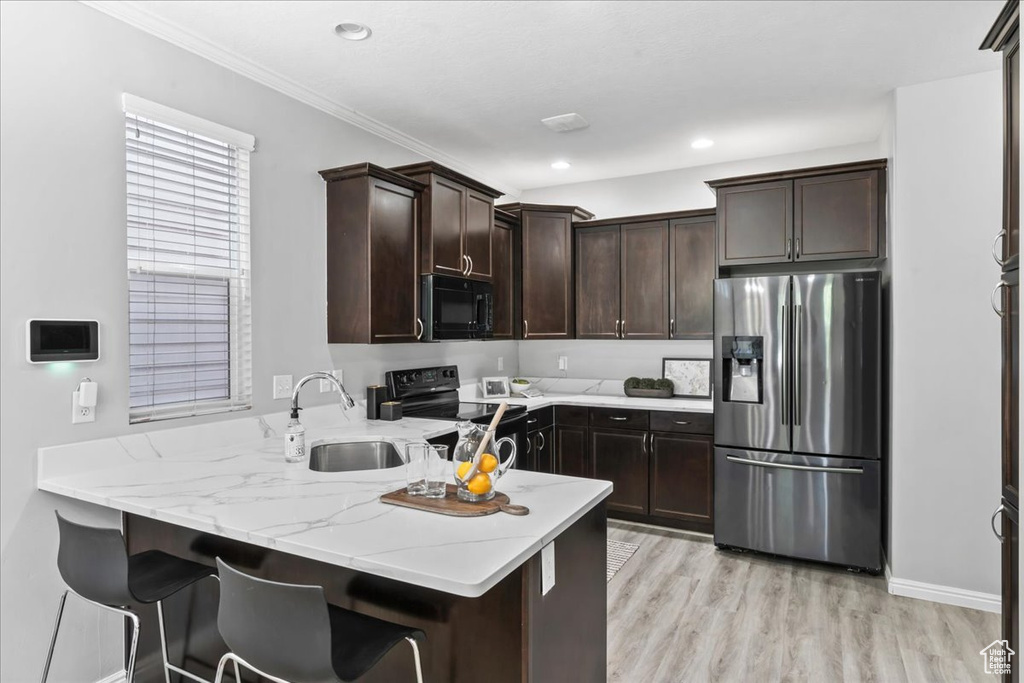 Kitchen with black appliances, a peninsula, dark brown cabinetry, light stone countertops, and light wood finished floors