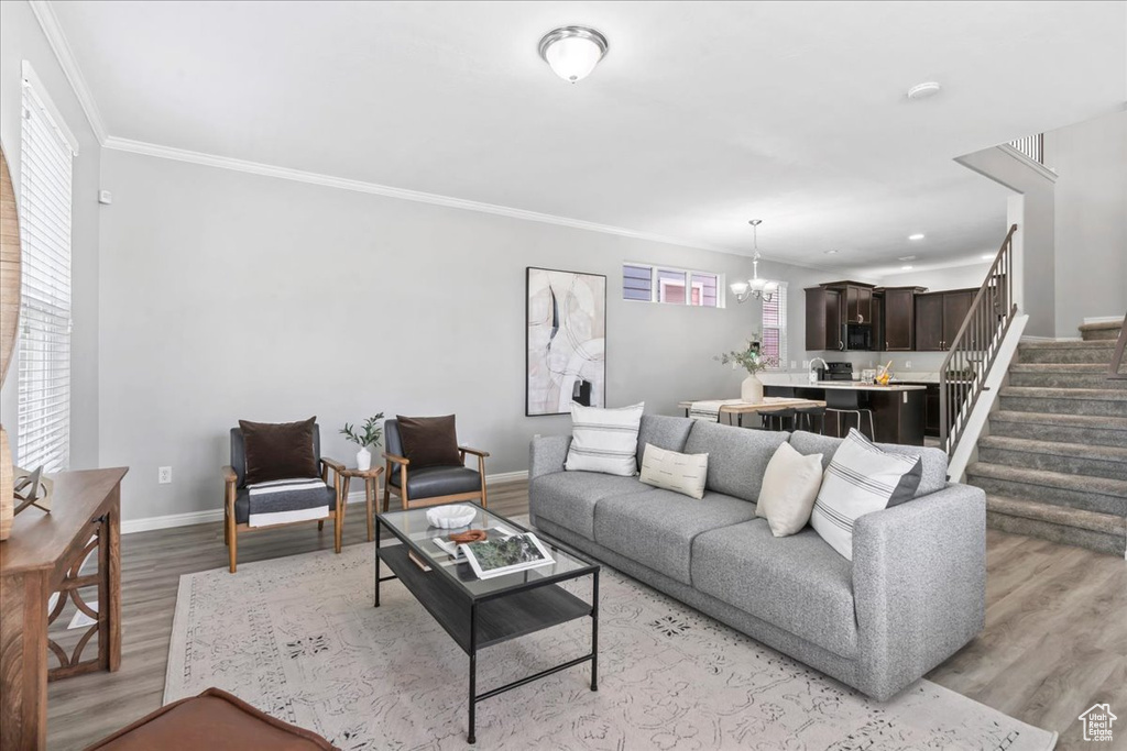 Living room featuring light wood finished floors, a chandelier, stairway, plenty of natural light, and crown molding