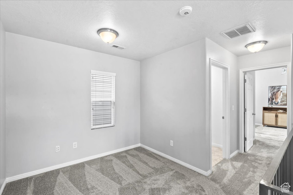 Empty room with carpet flooring, a textured ceiling, and a smoke detector