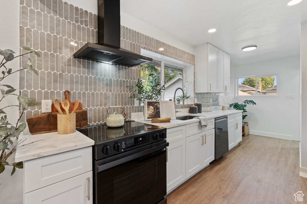 Kitchen with black / electric stove, wall chimney exhaust hood, dishwasher, decorative backsplash, and light wood finished floors