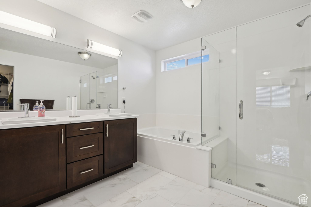 Bathroom featuring a stall shower, a garden tub, double vanity, and marble finish flooring