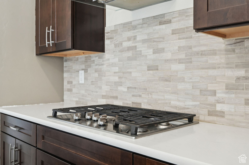 Kitchen with dark brown cabinets, stainless steel gas cooktop, light countertops, and tasteful backsplash