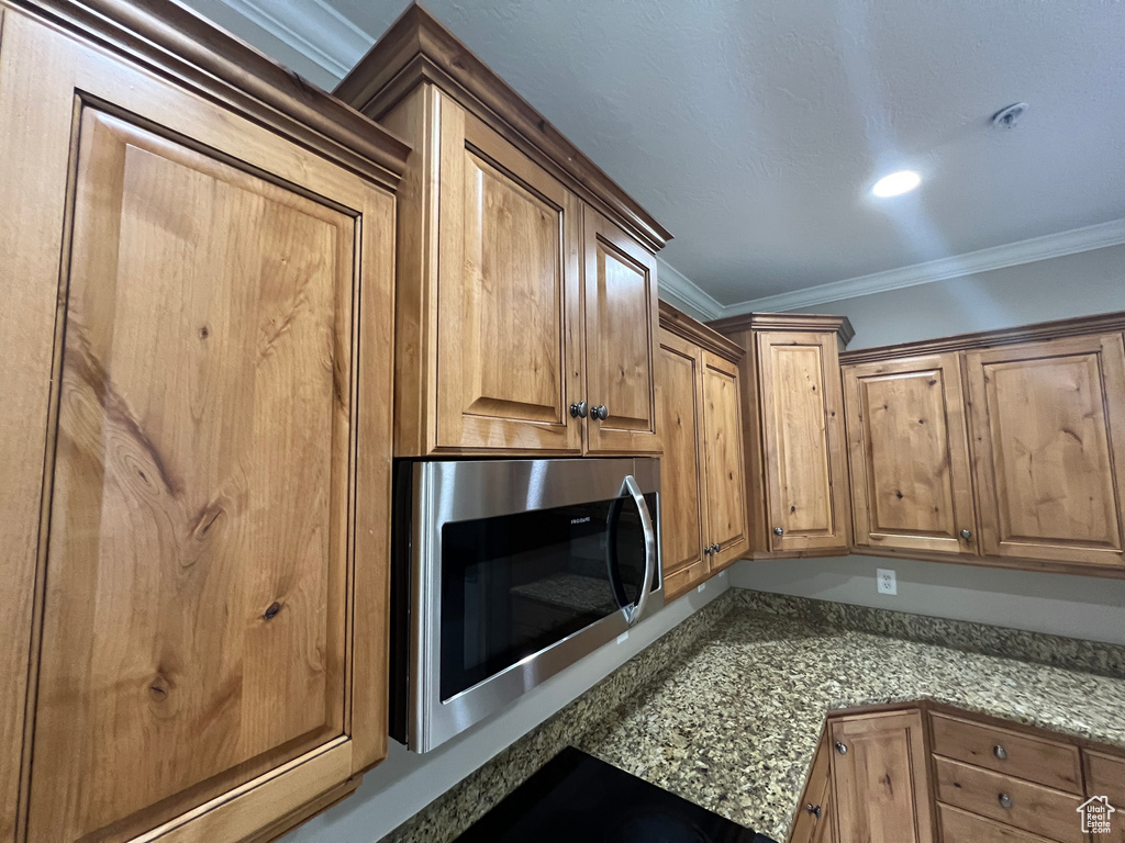 Kitchen view of stainless steel microwave, ornamental molding, light stone countertops, and brown cabinets