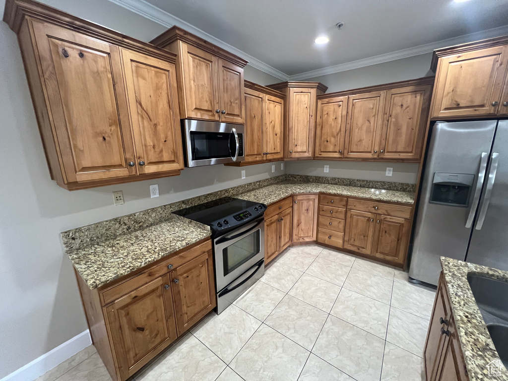 Kitchen with appliances with stainless steel finishes, ornamental molding, brown cabinets, stone countertops, and light tile patterned floors