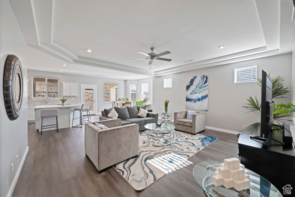 Living room with a tray ceiling, dark wood finished floors, ceiling fan, healthy amount of natural light, and recessed lighting