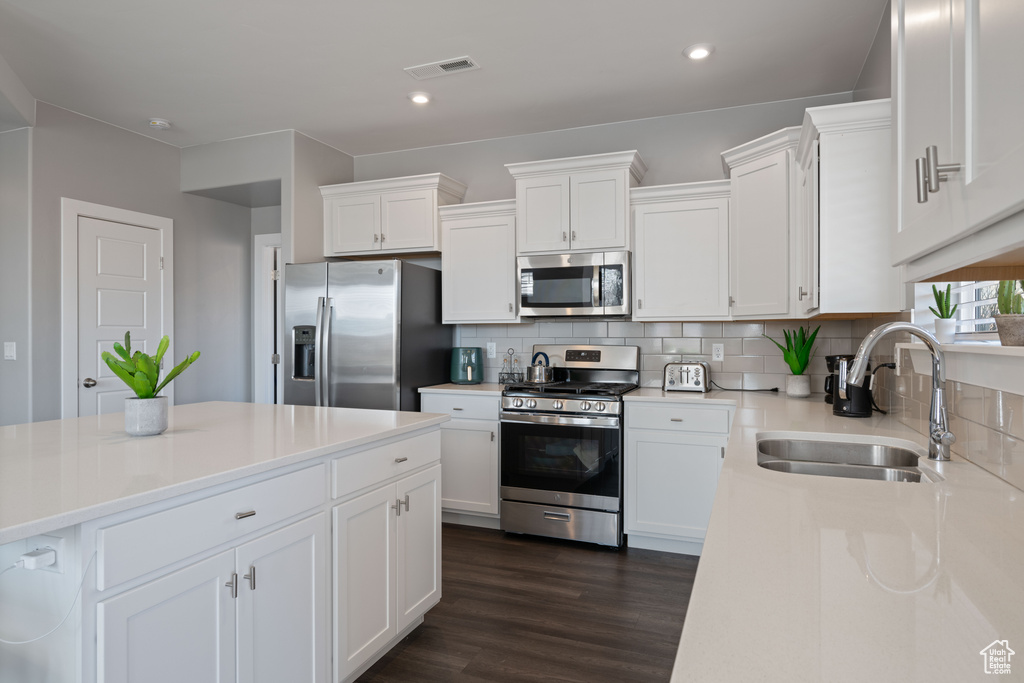 Kitchen featuring appliances with stainless steel finishes, dark wood-style flooring, white cabinetry, backsplash, and recessed lighting