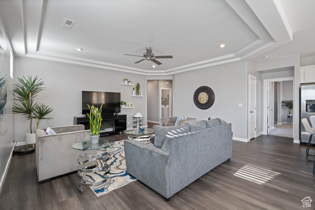 Living room with a raised ceiling, a ceiling fan, dark wood-style floors, and recessed lighting