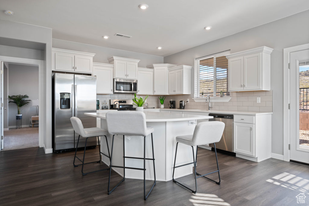 Kitchen with stainless steel appliances, a center island, dark wood-style flooring, white cabinetry, and decorative backsplash