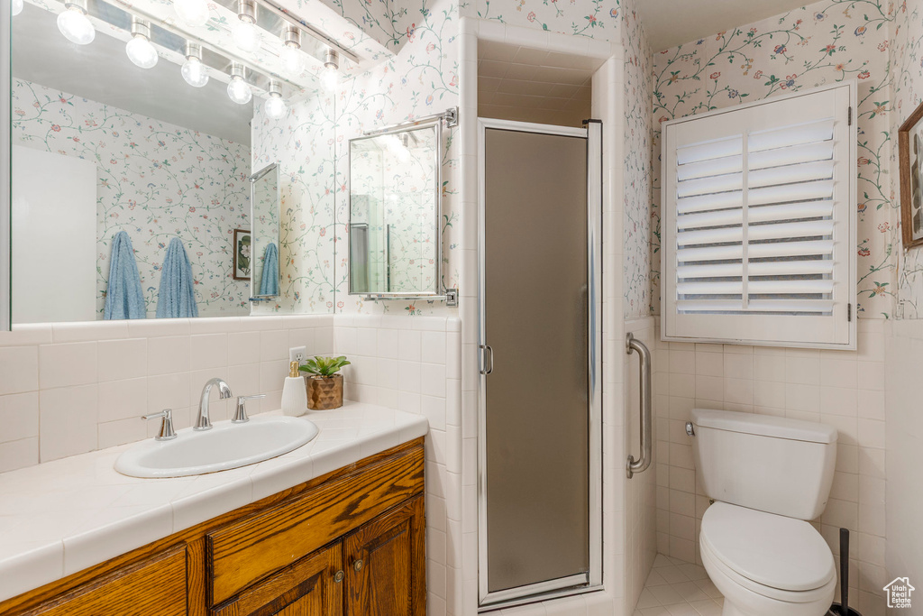 Bathroom featuring wallpapered walls, tile walls, vanity, a shower stall, and wainscoting
