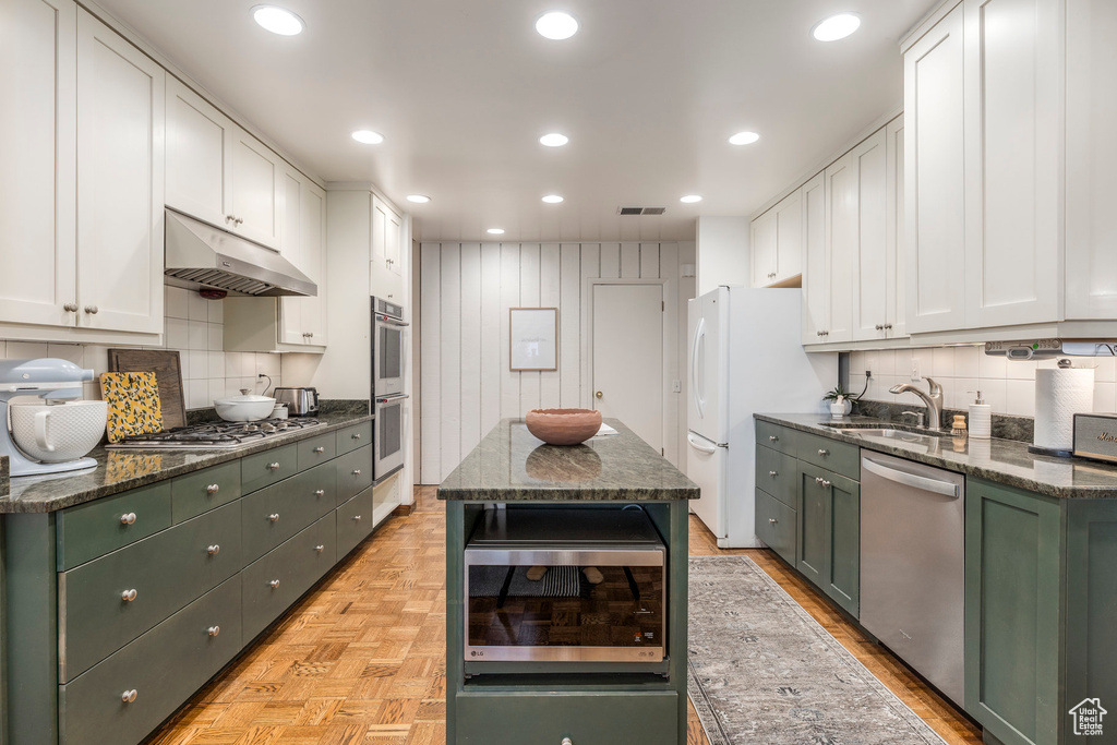Kitchen featuring appliances with stainless steel finishes, green cabinets, under cabinet range hood, white cabinets, and backsplash