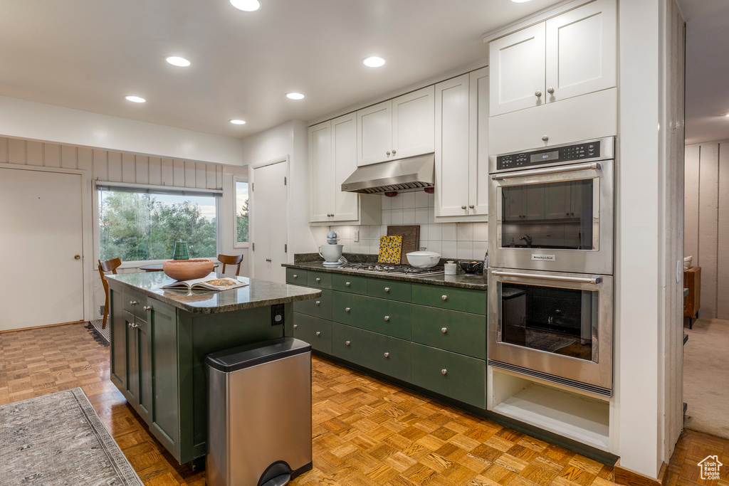 Kitchen featuring appliances with stainless steel finishes, under cabinet range hood, white cabinets, decorative backsplash, and a center island