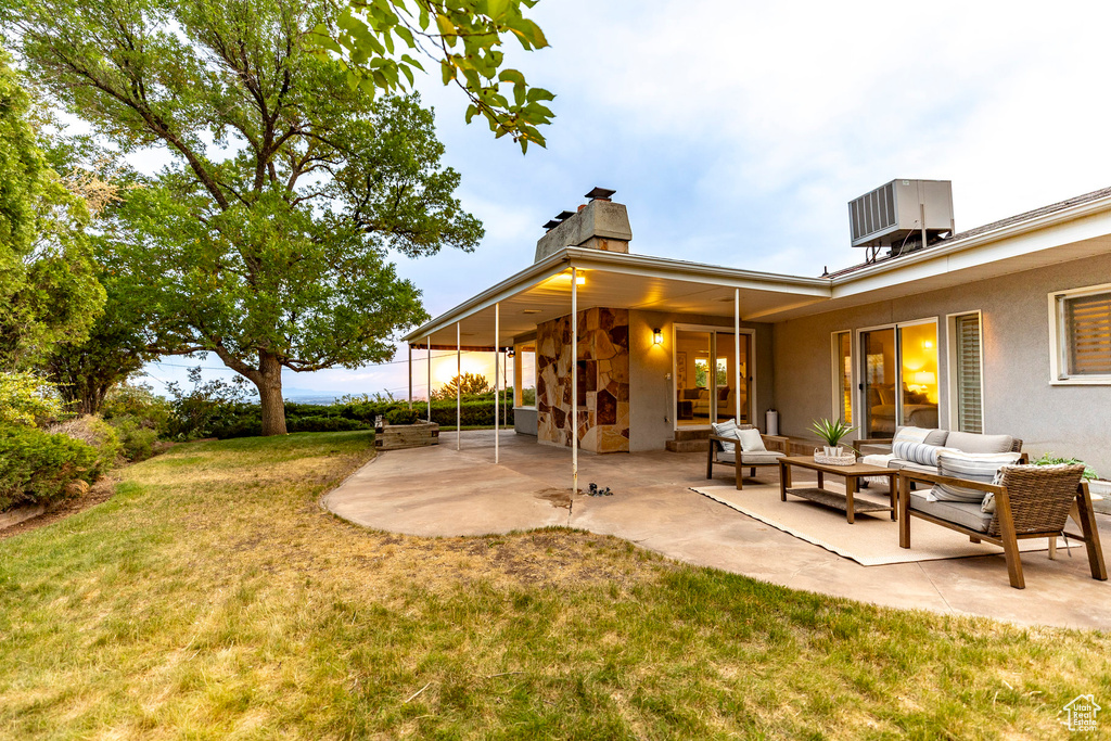 Back of property featuring a chimney, a patio, a lawn, an outdoor hangout area, and stone siding