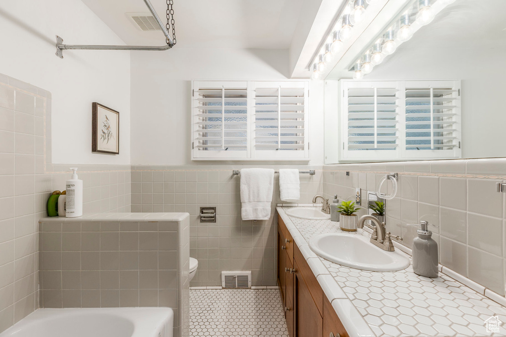 Full bath featuring tile walls, double vanity, a tub, tile patterned floors, and a wainscoted wall