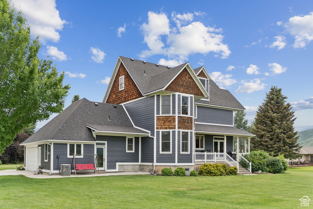 Back of house featuring covered porch, a lawn, an attached garage, and a patio