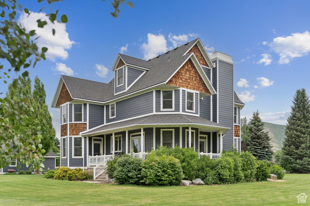 Rear view of property with a yard, covered porch, and a shingled roof