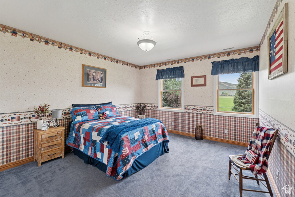 Carpeted bedroom with wallpapered walls, wainscoting, and a textured ceiling
