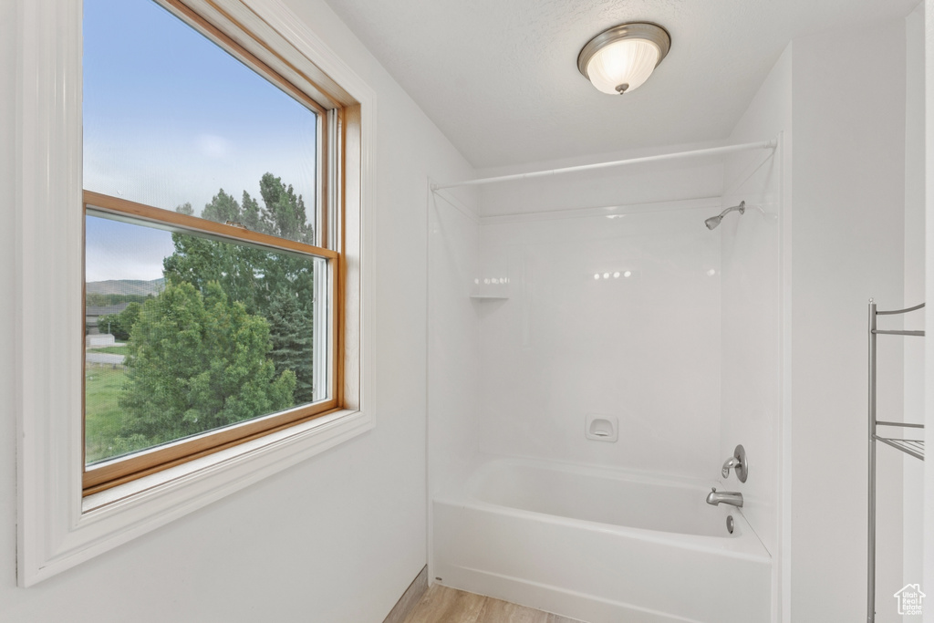 Full bath with washtub / shower combination, healthy amount of natural light, and wood finished floors