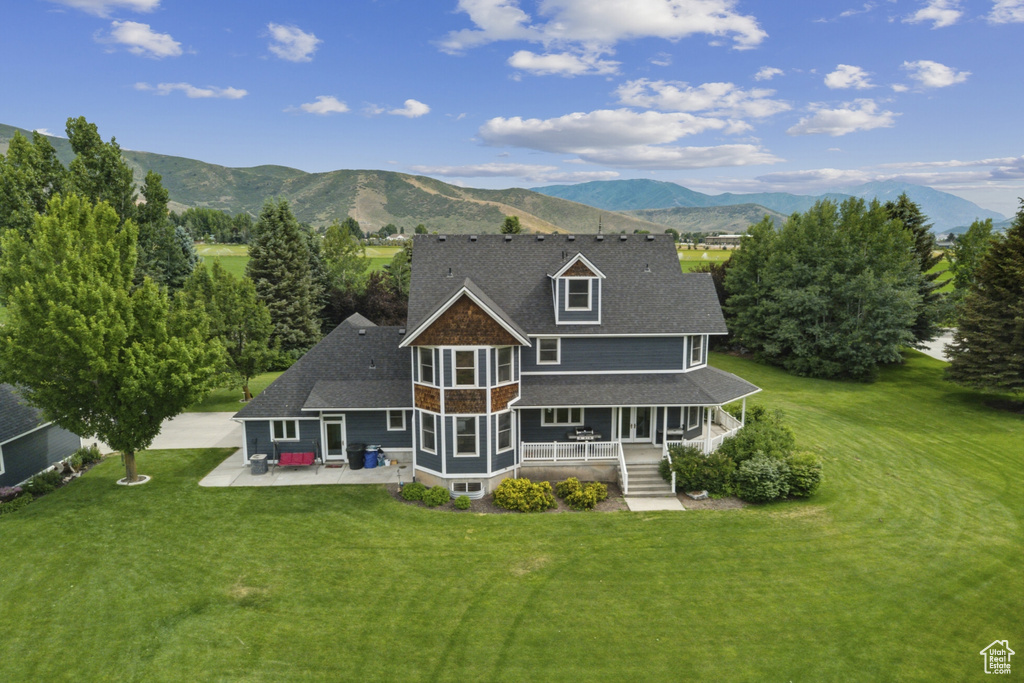 Rear view of property featuring a mountain view, a lawn, covered porch, a patio, and roof with shingles