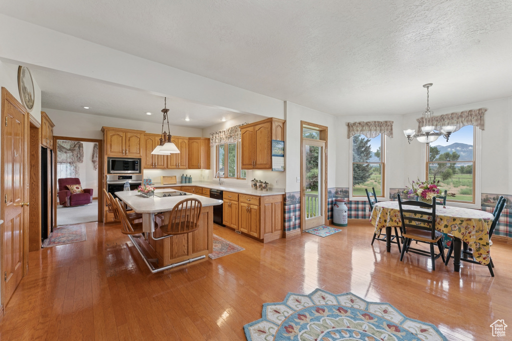 Kitchen with stainless steel appliances, light wood-style flooring, a kitchen island, light countertops, and a textured ceiling