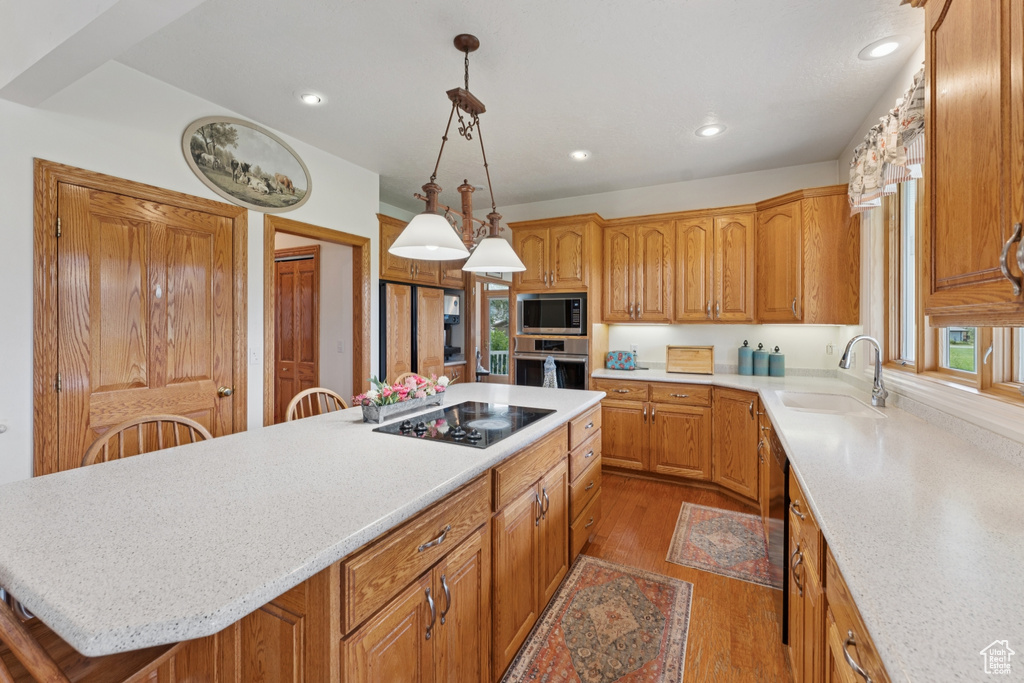 Kitchen featuring stainless steel appliances, a kitchen island, wood finished floors, recessed lighting, and hanging light fixtures