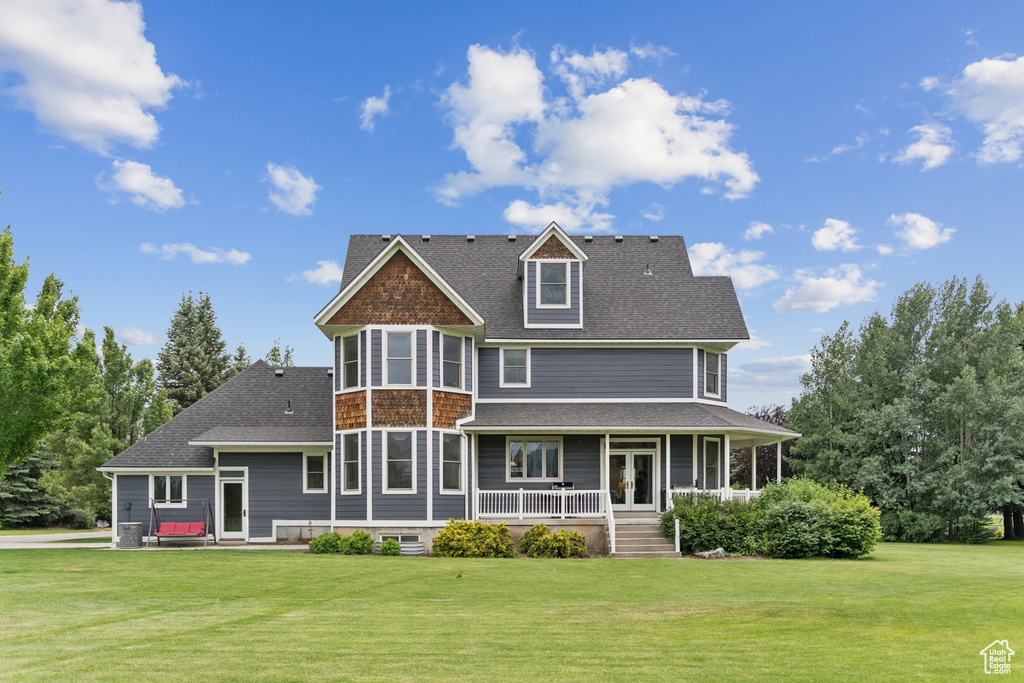 Back of property with a porch, a yard, and roof with shingles