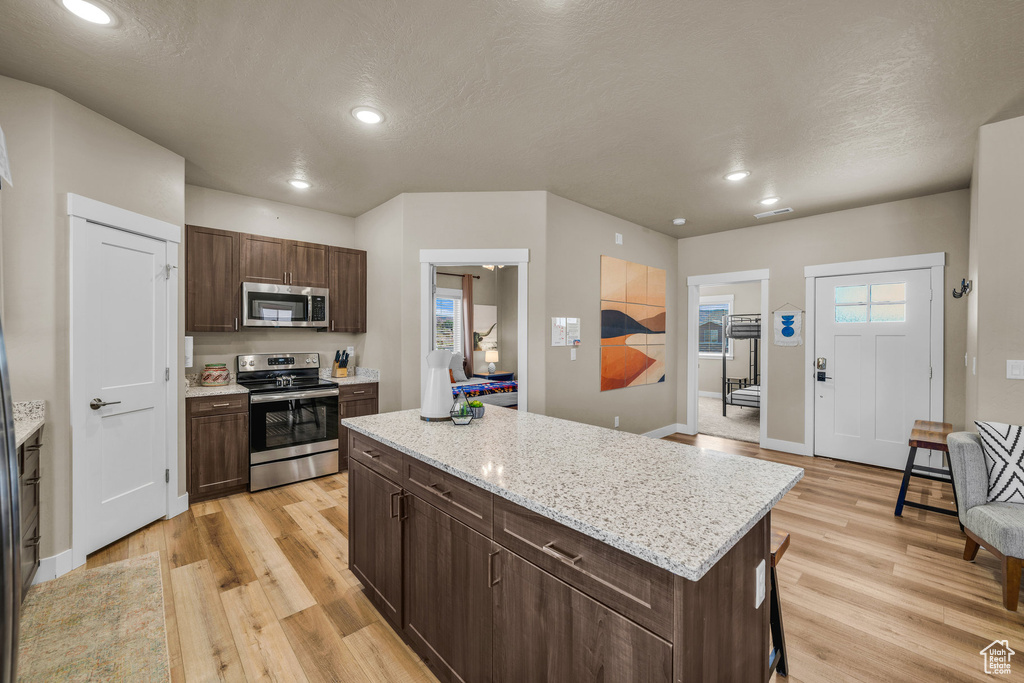 Kitchen featuring appliances with stainless steel finishes, light wood-style floors, a center island, recessed lighting, and dark brown cabinetry