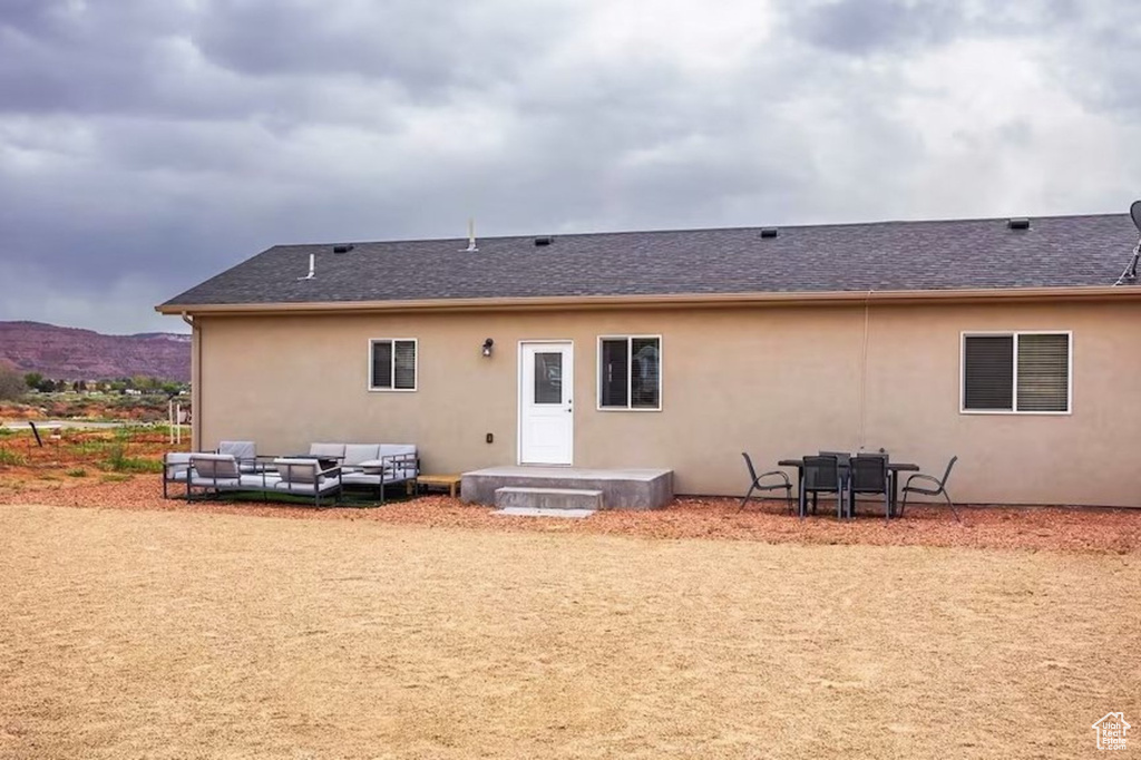 Back of property featuring stucco siding, a patio, outdoor lounge area, a shingled roof, and a mountain view