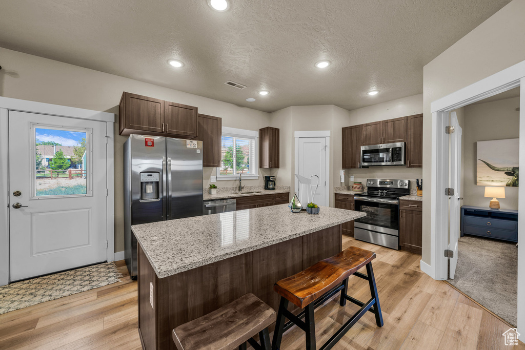 Kitchen featuring appliances with stainless steel finishes, dark brown cabinets, a kitchen island, a breakfast bar area, and recessed lighting