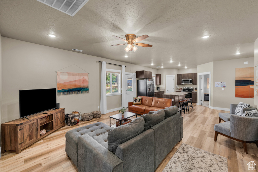 Living room with ceiling fan, light wood-style floors, recessed lighting, and a textured ceiling