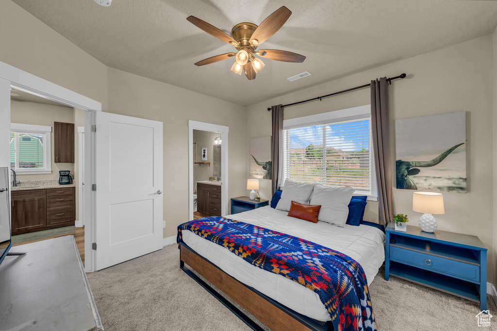 Bedroom featuring light colored carpet, ensuite bath, multiple windows, and ceiling fan