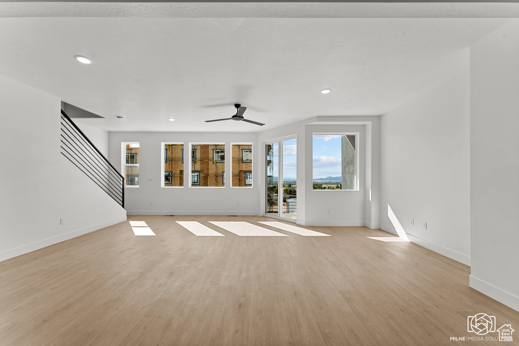Unfurnished living room with light wood finished floors, ceiling fan, recessed lighting, and stairs