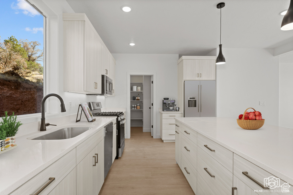 Kitchen with stainless steel appliances, light countertops, light wood-style flooring, hanging light fixtures, and recessed lighting