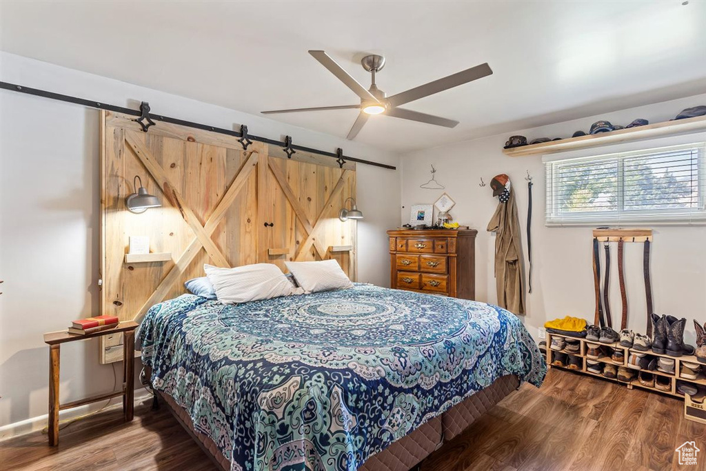 Bedroom with a barn door, wood finished floors, and a ceiling fan