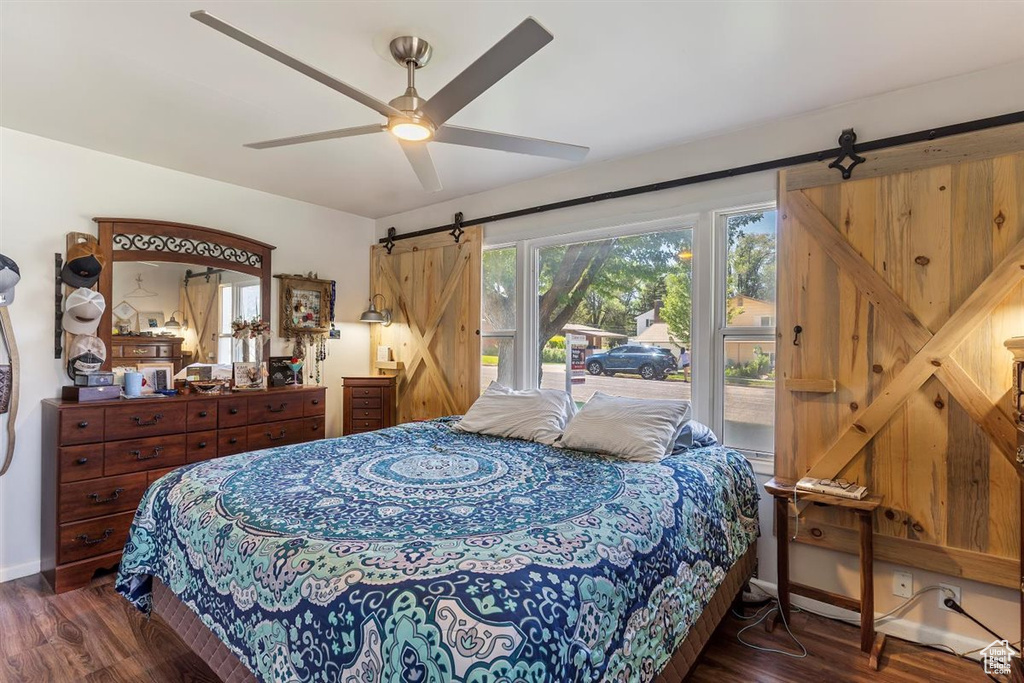 Bedroom with a barn door, access to exterior, wood finished floors, and a ceiling fan