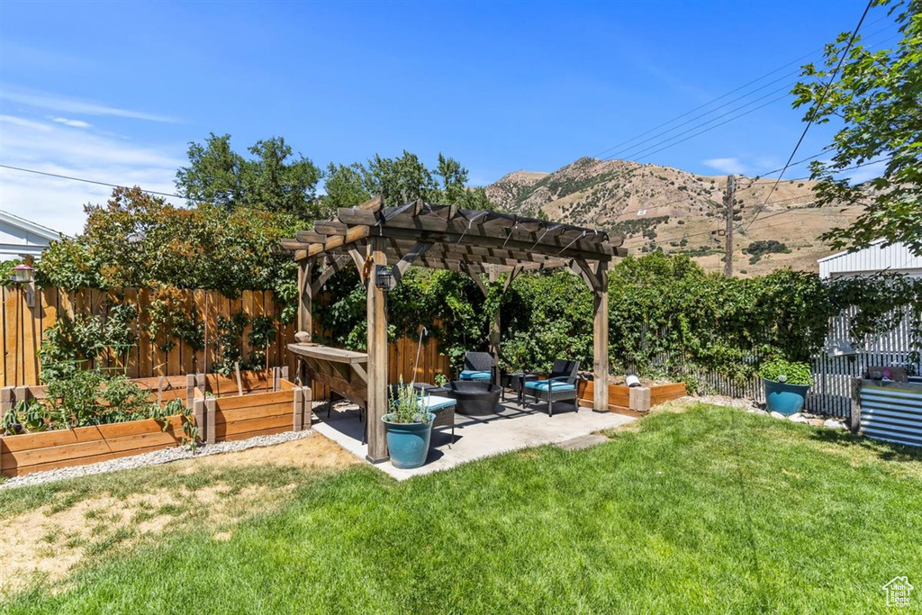 Fenced backyard featuring a vegetable garden, a patio area, a mountain view, a pergola, and an outdoor hangout area