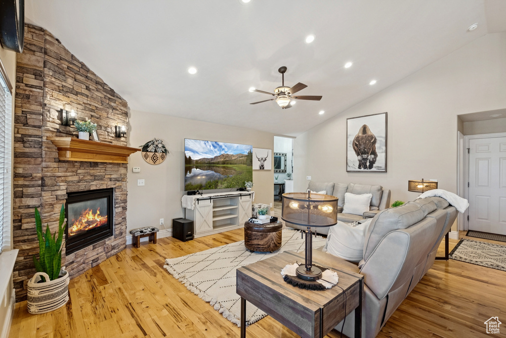 Living room with a stone fireplace, light wood finished floors, ceiling fan, high vaulted ceiling, and recessed lighting