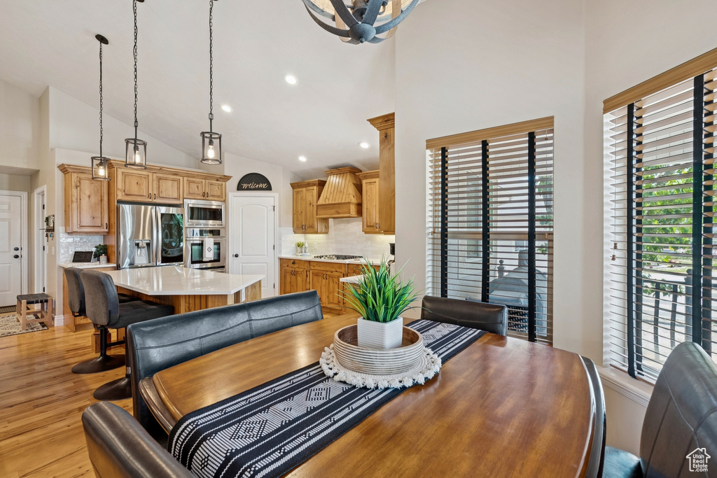 Dining space with high vaulted ceiling, light wood-type flooring, recessed lighting, and a chandelier